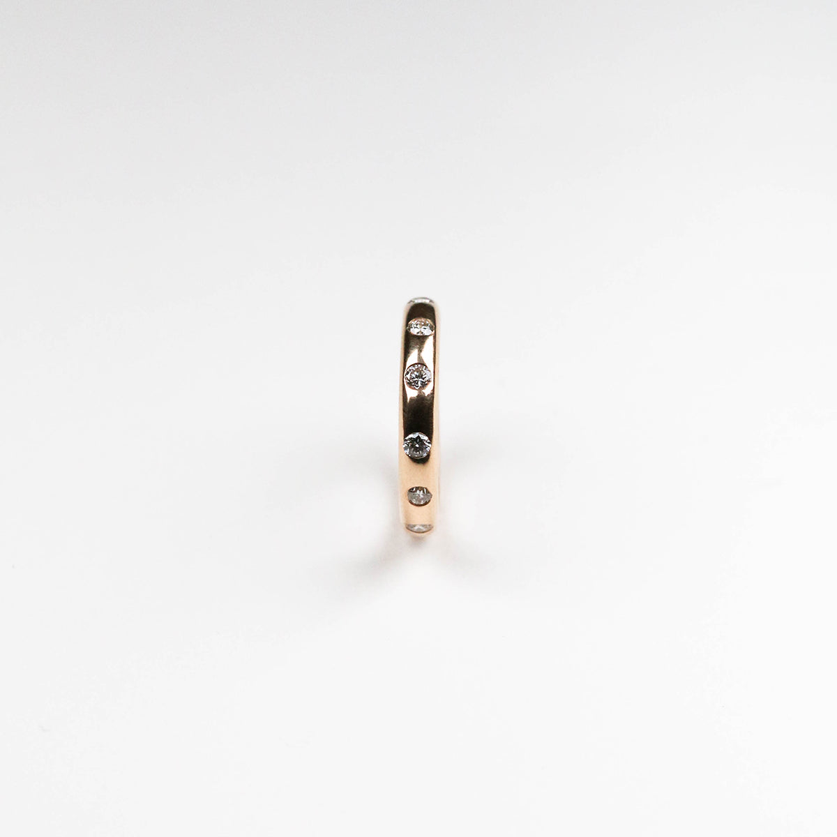 Pictured from the side, showing the diamonds around the circumference of the ring. An excellent choice for those who prefer minimalist wedding ring design. This beautiful eternity ring is handmade in 18ct rose gold and flush set with twelve .05pt brilliant-cut white diamonds totalling 60pt. Measuring 3.5mm wide and 1.8mm in depth.