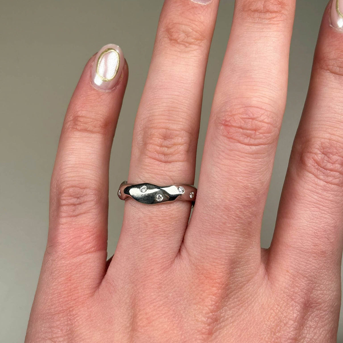 Pictured on a ring finger, this unique platinum eternity band measures 4.5mm in width and is set with 12 white diamonds decorated all around the band, totalling .25 points of a carat.  From signature Carved collection, handmade platinum eternity ring from Jeremy's signature collection.