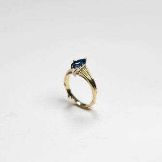 This remarkable piece features a 2.5mm wide band, intricately hand-carved from luxurious 18ct yellow gold. The band is adorned with a delicate vine design, symbolising the natural beauty and elegance that define Jeremy Hoye's jewellery. At its heart lies a stunning 1.25ct marquise blue sapphire, set to capture and reflect light beautifully.