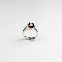 Hand carved in solid silver and finished with textured inlaid detail. This ring holds a rich, round garnet which sits asymmetrically on the finger.