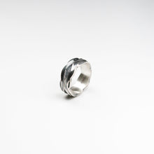 This handmade silver band boasts a 8mm width. Its appeal lies in the fluid oval design with textured inlay, reflecting the unique craftsmanship characteristic of handmade jewellery.