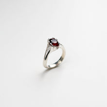 Hand carved in solid silver and finished with textured inlaid detail. This ring holds a rich, round garnet which sits asymmetrically on the finger.