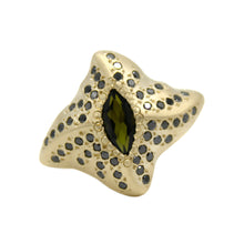 The ring features a central marquise green tourmaline and 50pts of black diamonds on each wing plate to maximise sparkle from every angle. Hand-crafted in 9ct yellow gold.