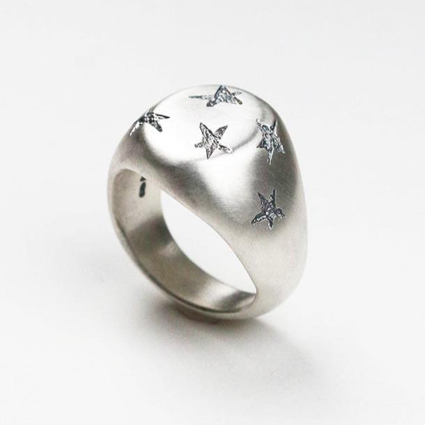 Handmade in silver with scattered inlaid textured star shapes, this ring is designed as an alternative to the traditional style signet ring. the top measures 12mm by 10mm.