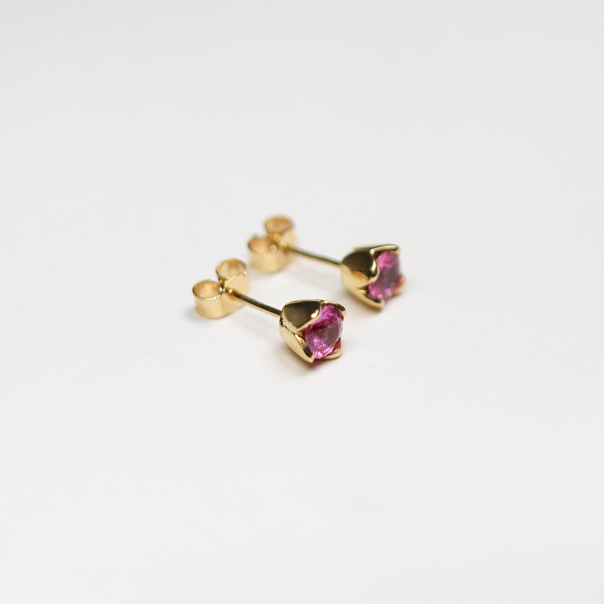 Handmade in 18ct yellow gold and set with two round pink sapphires totalling 1.10ct.